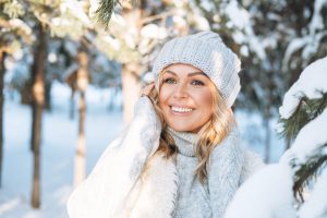 portrait of smiling blonde woman hands near face against background of snowy winter forest